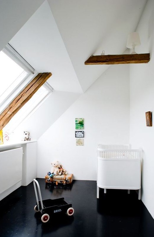 a contrasting attic nursery with a black floor, wooden beams, a white crib, some toys and a bright galley wall