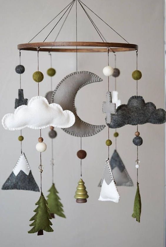 a cool woodland nursery mobile with mountains, pompoms, trees, clouds, crosses and a half moon is a stylish forest-inspired idea