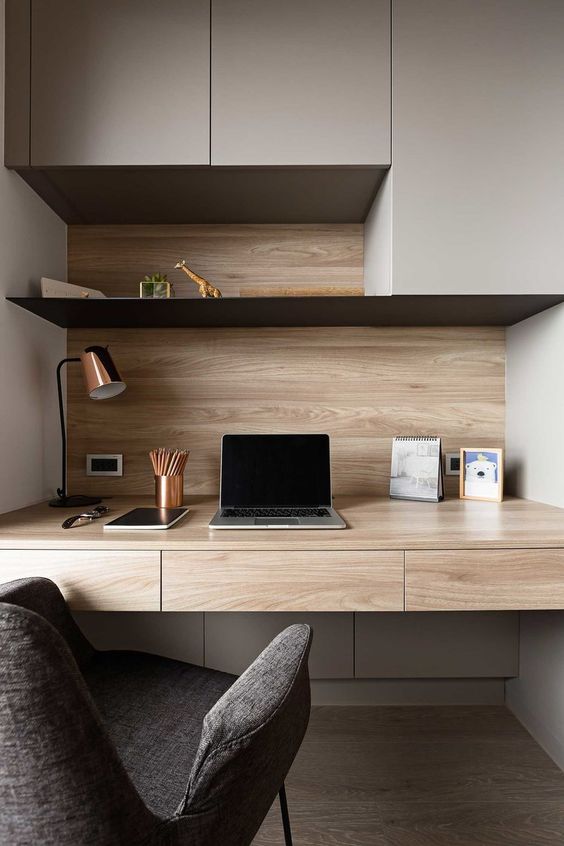 A cozy minimalist home office with sleek storage units, an open shelf and a built in desk, a comfy chair and a copper table lamp