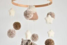 a cozy neutral and pastel mobile of felt and yarn, with a bear in a scarf, pompoms, stars and a mountain is a lovely idea for a mountain-themed space