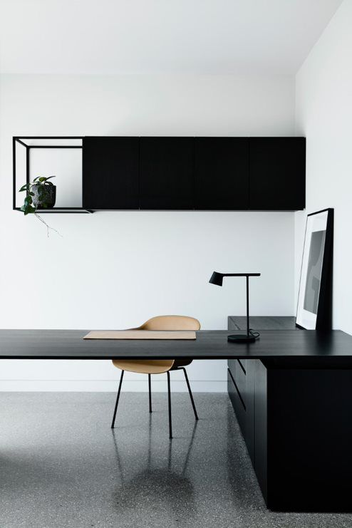 a dramatic minimalist home office with a large corner desk with storage, a black table lamp and a sleek storage unit with an open compartment