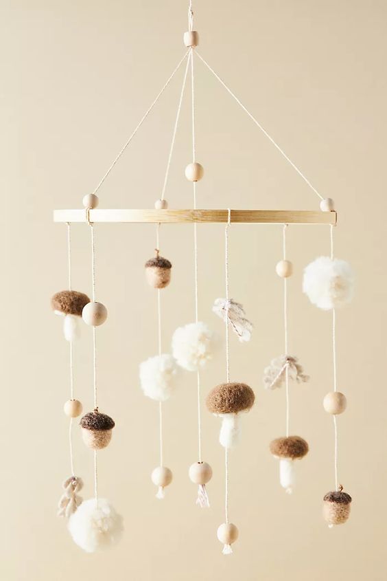 a fall-themed nursery mobile with pompoms, wooden beads, mushrooms and acorns is a cool and chic idea