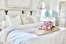 a gorgeous shabby chic bedroom in white, with a wooden bed and an artwork, a mint screen, a fan, neutral bedding with ruffles