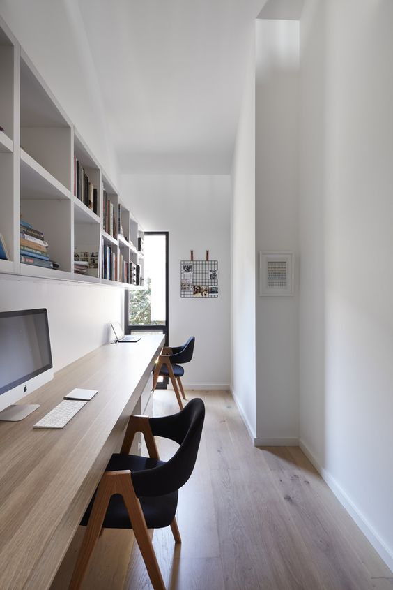 a long and narrow minimalist home office with shelving units and a floating double desk, comfy black chairs and much natural light