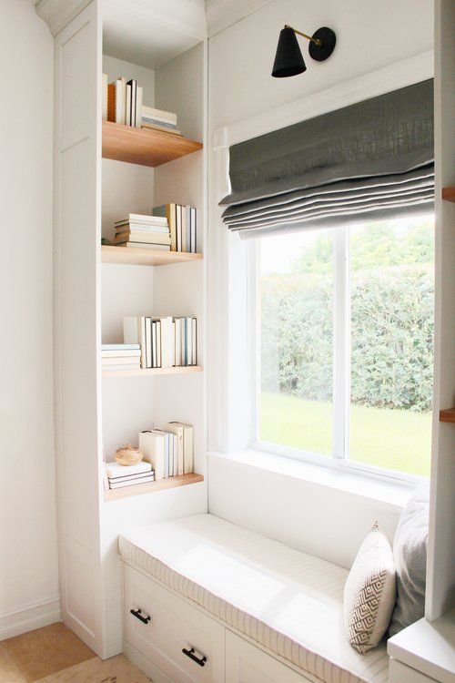 A lovely reading nook with built in shelves, an upholstered windowsill daybed, a graphite grey Roman shade for blocking out the sun