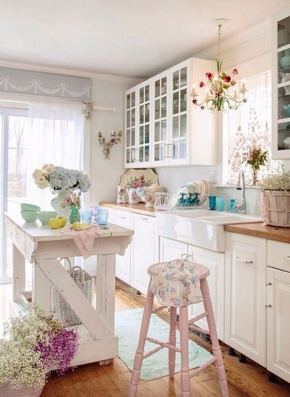 a lovely shabby chic kitchen with white cabinets, pastel pink touches, floral prints, a kitchen island and French doors