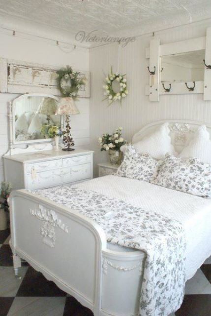 a lovely white shabby chic bedroom with refined furniture, floral bedding, a mirror on the wall, white blooms and a floral lamp