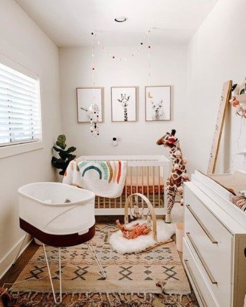 A mid century modern meets boho nursery with layered rugs, a crib with bright bedding, an additional crib, a white dresser and a gallery wall