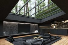 a minimalist conversation pit in black with a large sofa and pillows, a couple of coffee tables and a skylight through which you can see the trees