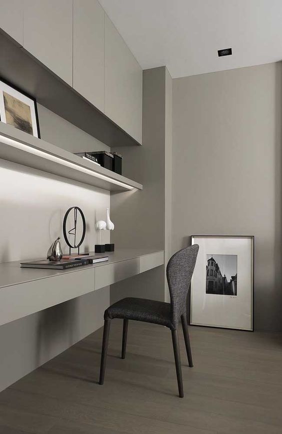 A minimalist grey home office with a sleek storage unit and a built in shelf and desk with storage, a grey chair and some lovely artworks