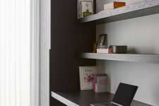 a minimalist home office with a sleek storage unit, open shelves, a built-in desk and a black chair plus greenery in a vase
