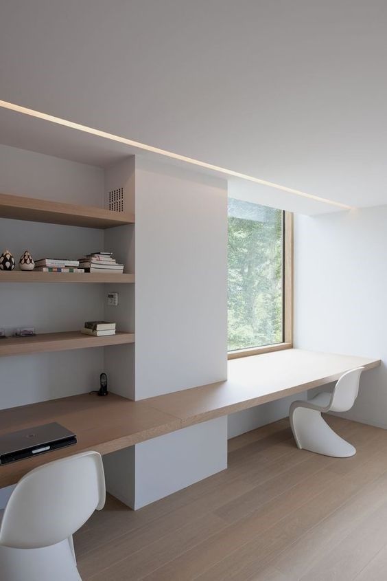 A minimalist home office with built in shelves, a floating desk and sculptural chairs plus a window with a view