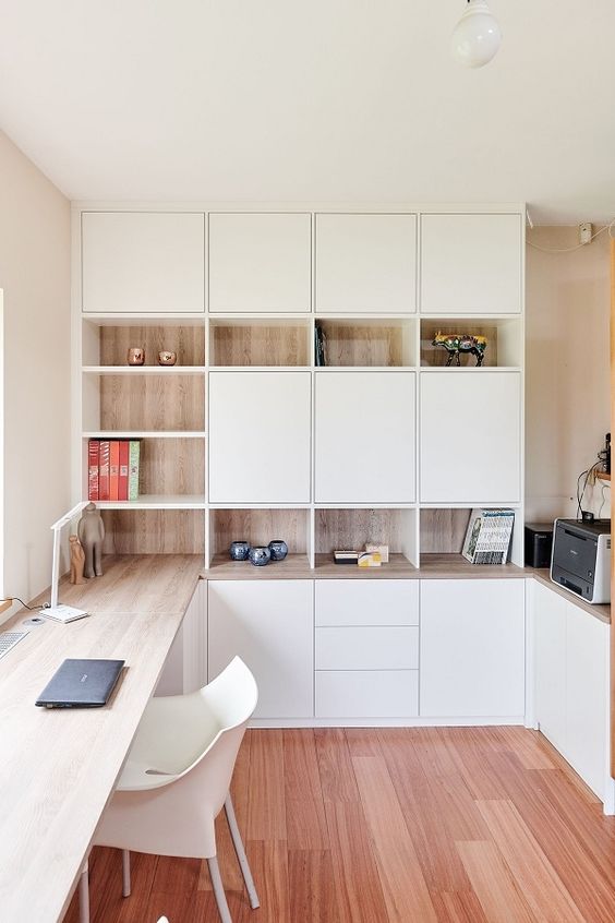 A minimalist home office with white and stained storage units, with a built in desk and some pretty decor is very chic