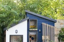 a navy playhouse with a planked porch and a wall-mounted seat, potted greenery looks like a real mid-century modern house