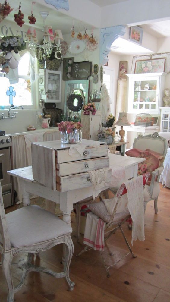 a neutral and pastel shabby chic kitchen and dining space with curtains on the cabinet, lots of floral prints, refined furniture and hanging lamps
