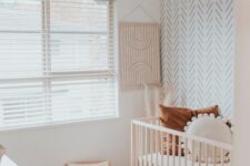 a neutral boho nursery with a white dresser, a stained crib, a tiny rocker for the baby, an accent wall and a printed rug