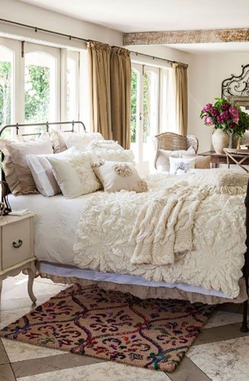 a neutral shabby chic bedroom with a metal bed, refined neutral furniture, ruffle and lace bedding and potted blooms