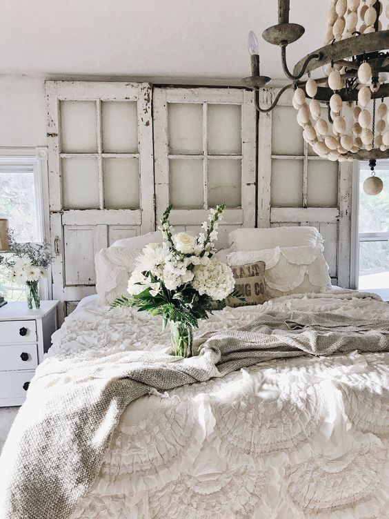 a neutral shabby chic bedroom with vintage doors instead of a headboard, ruffle and lace bedding, a bead chandelier and blooms