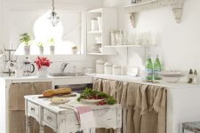 a neutral shabby chic kitchen with cabinets with burlap hanging, a shabby kitchen island, refined shelves and potted greenery
