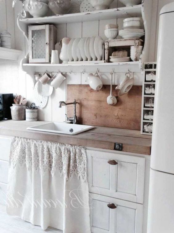 a neutral shabby chic kitchen with vintage cabinets, open shelving, stained countertops and a backsplash, a lace curtain for covering