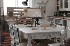 a neutral shabby chic kitchen with white cabinets and glass ones, a vintage table and chairs, metal retro lamps and aqua-colored clocks