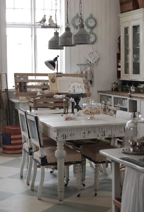 A neutral shabby chic kitchen with white cabinets and glass ones, a vintage table and chairs, metal retro lamps and aqua colored clocks