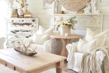 a neutral shabby chic living room with white walls, a shabby sideboard, a wooden clock and a table and some textiles