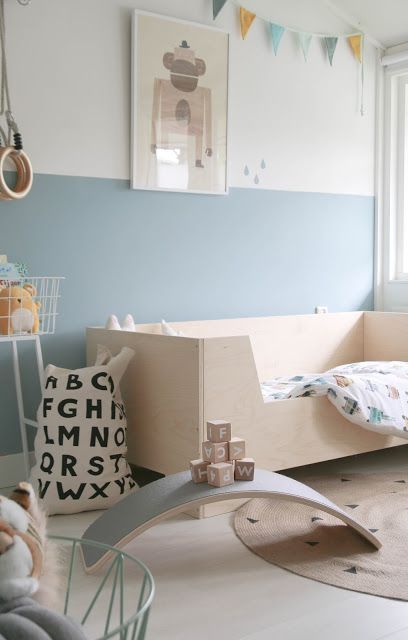a pastel Scandinavian kid's room with a plywood bed, color block blue walls, a colorful bunting, a printed fabric bag for storage and stylish toys