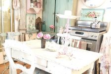 a pastel shabby chic kitchen with pastel blue and pink cabinets, a white table, floral chairs and linens plus a couple of crystal chandeliers