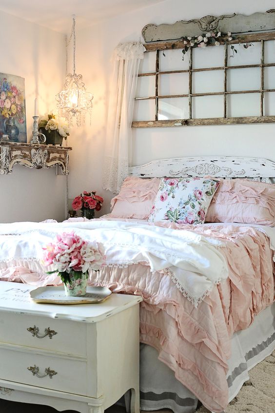 a refined shabby chic bedroom with an old window frame, white shabby furniture, a crystal pendant lamp and pink and floral bedding