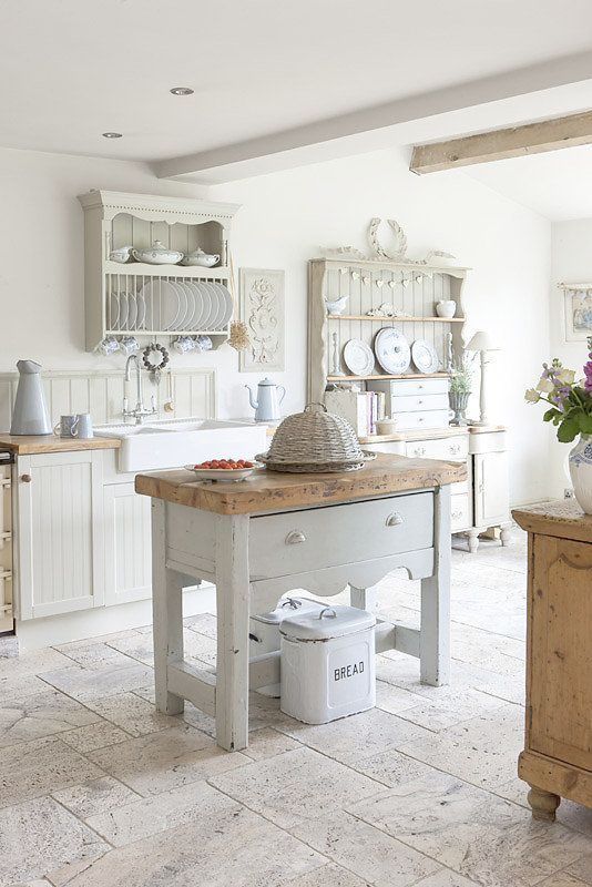 A romantic neutral shabby chic kitchen with beadboard cabinets, an off white kitchen island and refined open storage units