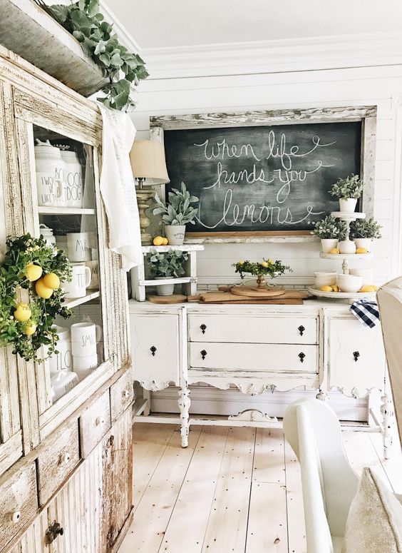 a romantic neutral shabby chic kitchen with refined furniture, a chalkboard, potted greenery and lemons for a touch of color