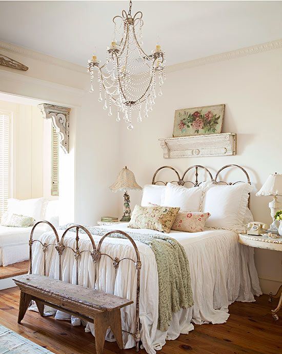a romantic shabby chic bedroom with a forged bed, a crystal chandelier, chic lamps and artworks