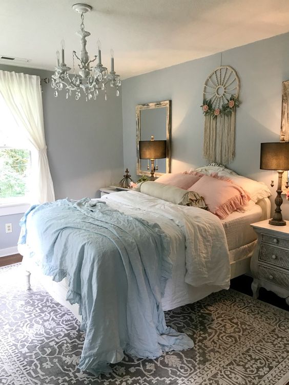 a romantic shabby chic bedroom with pastel blue walls, a dream catcher, refined furniture, a crystal chandelier and ruffled bedding