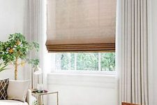 a semi sheer burlap Roman shade paired with creamy curtains makes the window look cooler and allows to keep the space private when needed