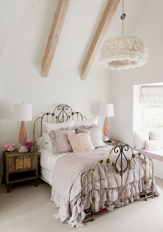 a shabby chic bedroom with a shabby forged bed, stained wooden furniture, a fluffy pendant lamp and pastel bedding