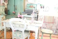 a shabby chic kitchen with neutral shabby furniture, floral textiles and linens, an aqua sideboard and a pink shelving unit