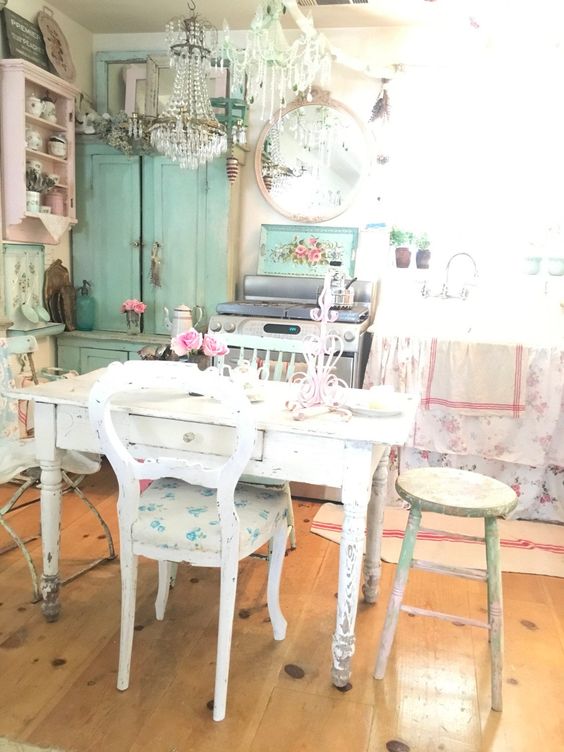 a shabby chic kitchen with neutral shabby furniture, floral textiles and linens, an aqua sideboard and a pink shelving unit