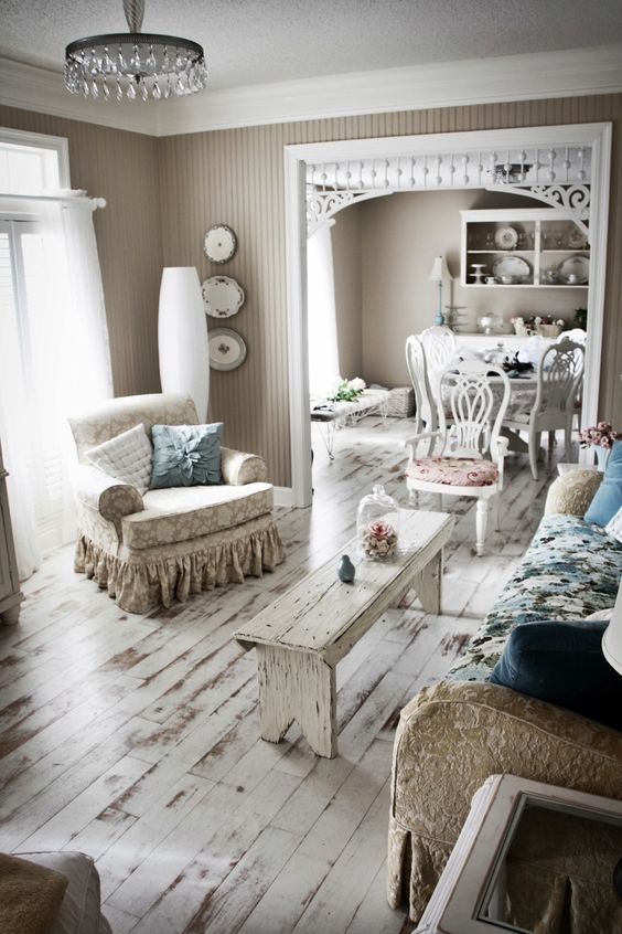 a shabby chic living room with a blue floral sofa, printed chairs and a white bench, a crystal chandelier and pastel pillows