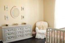 a shabby chic nursery with tan walls, elegant grey furniture, a white chair, a pretty vintage chandelier and a gallery wall with mirrors