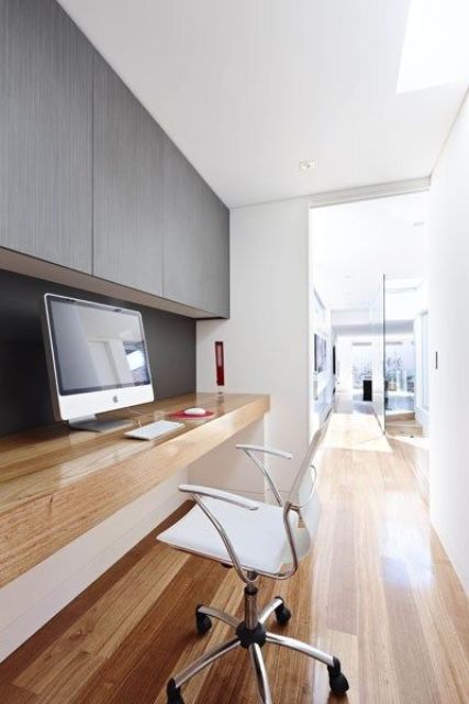 A sleek minimalist home office space with a sleek storage unit, a built in desk, a white chair and a PC are all you need for working