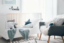 a small Scandinavian nursery with a white crib, a grey chair, pastel pillows and textiles, some artwork and layered rugs plus poufs
