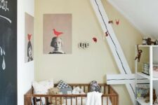 a small attic nursery with a catchy artwork, a chalkboard door, a simple crib and a storage unit for a modern look