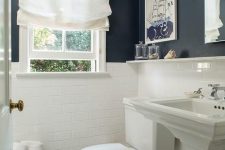 a small bathroom with black and white walls, white appliances, art and a white Roman shade that brings a traditional feel to it