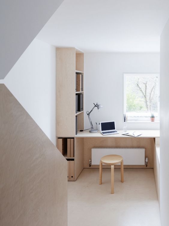 A small minimalist home office nook with a view, a built in plywood storage unit, a built in desk and a stool is chic and comfortable
