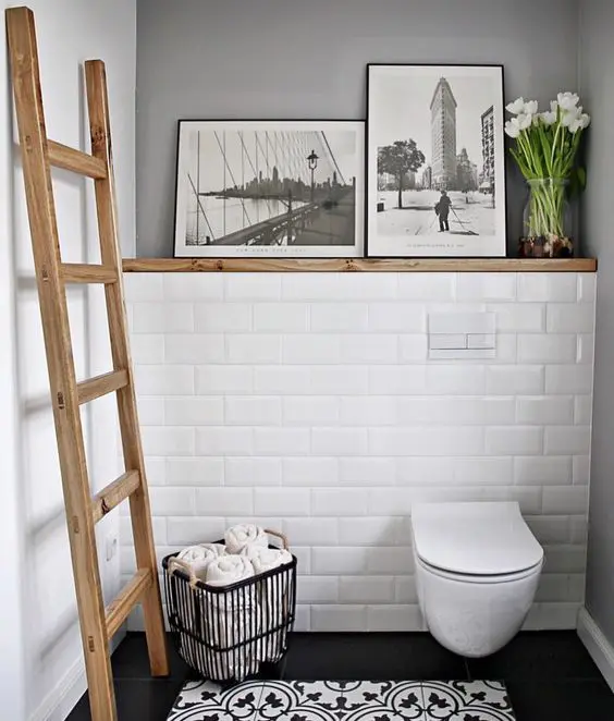 a small monochromatic powder room accented with a wooden ladder and a ledge with artworks and blooms looks warmer and cooler