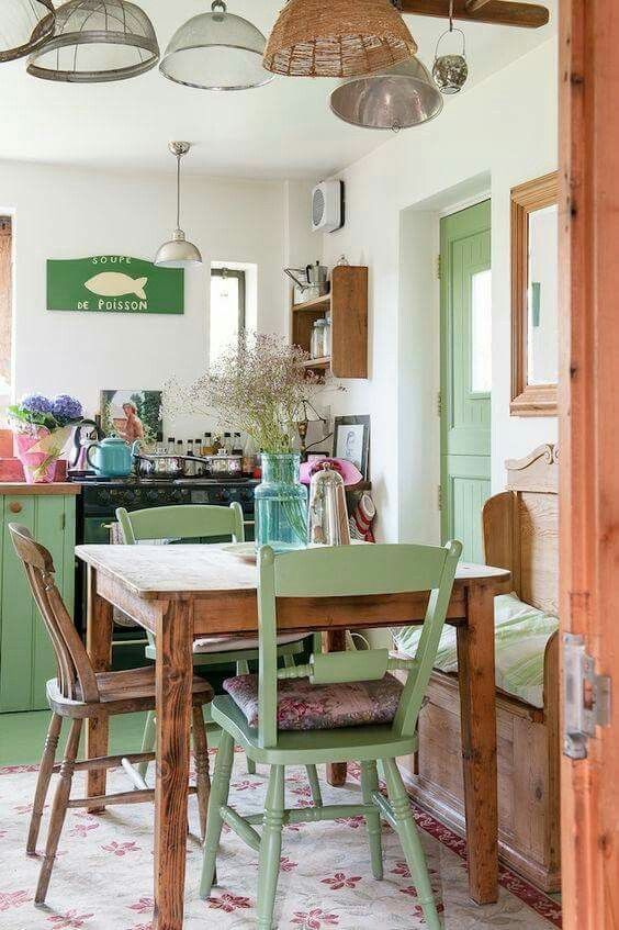 a small shabby chic kitchen with green furniture, metal and woven lamps, a wooden table and storage units and blooms