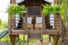a stained kids’ playhouse with low chairs, potted greenery, lights, a chalkboard and a ladder will be great for adults, too