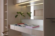a stylish minimalist home office nook with light stained plywood furniture, a built-in desk and lights, a comfortable chair and a mirror
