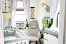 a tiny and lovely nursery in neurrals, with a stylish crib and dresser, a grey chair, some neutral bedding and faux taxidermy